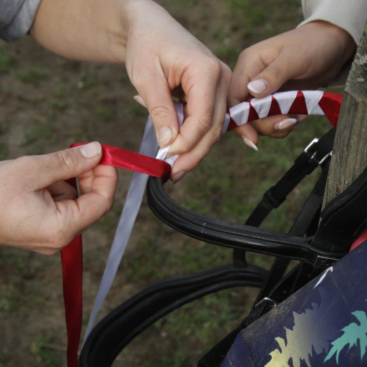 Two Horse Rangers working together, winding red and white ribbon around a bridle held on a fence post