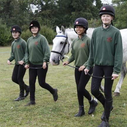 Four Horse Rangers in green jumpers and riding hats walking a dappled grey horse across the field.